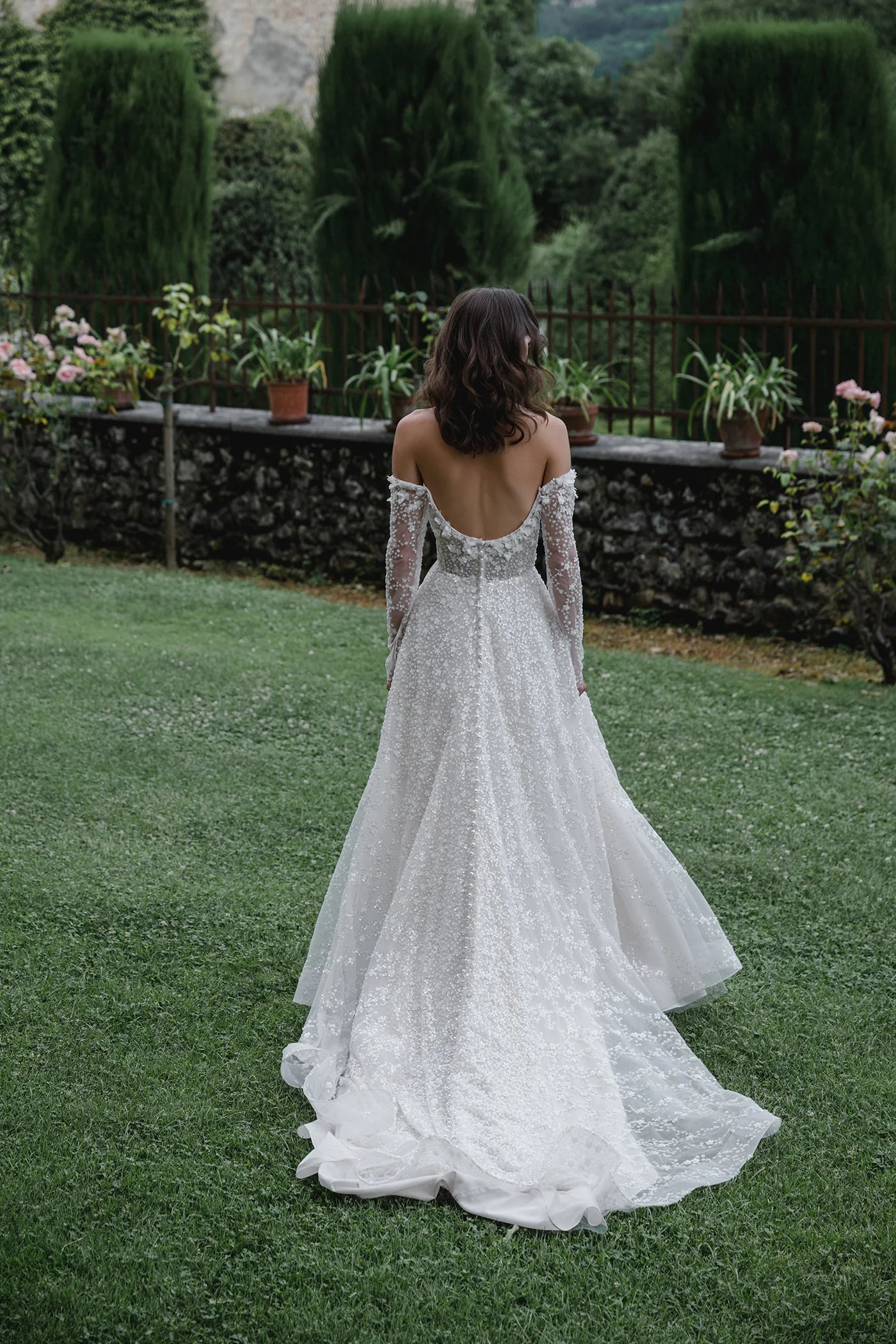Woman in a white lace wedding dress standing in a garden.