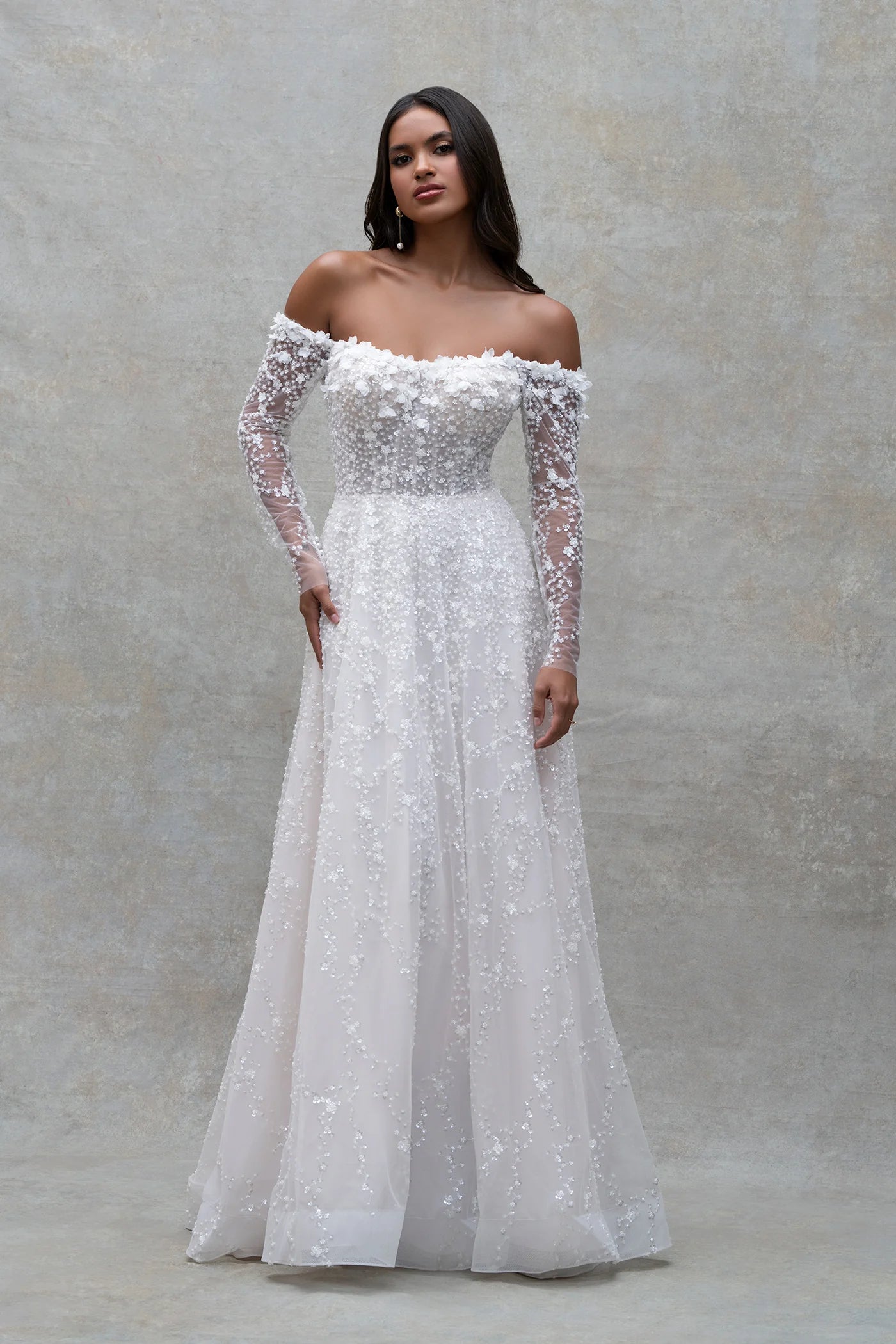 Woman wearing a white off-shoulder gown with long sleeves against a gray background