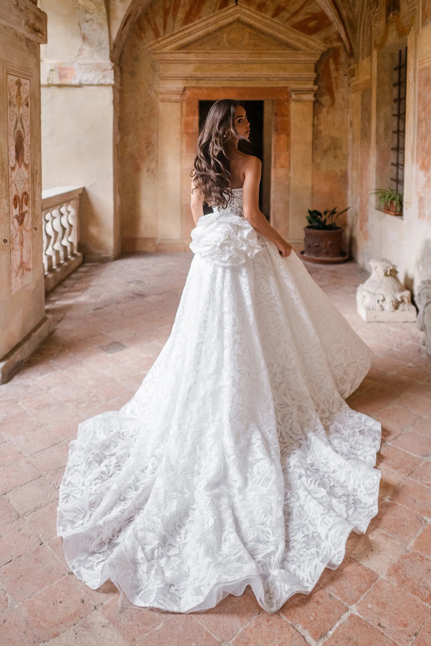 Woman in a white lace wedding dress standing in an elegant hallway.