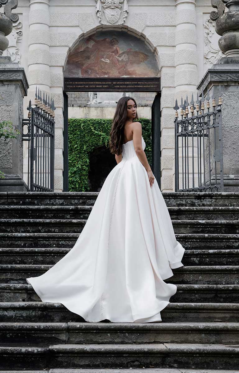 Woman in a white wedding dress standing on stone steps in front of an elegant building.