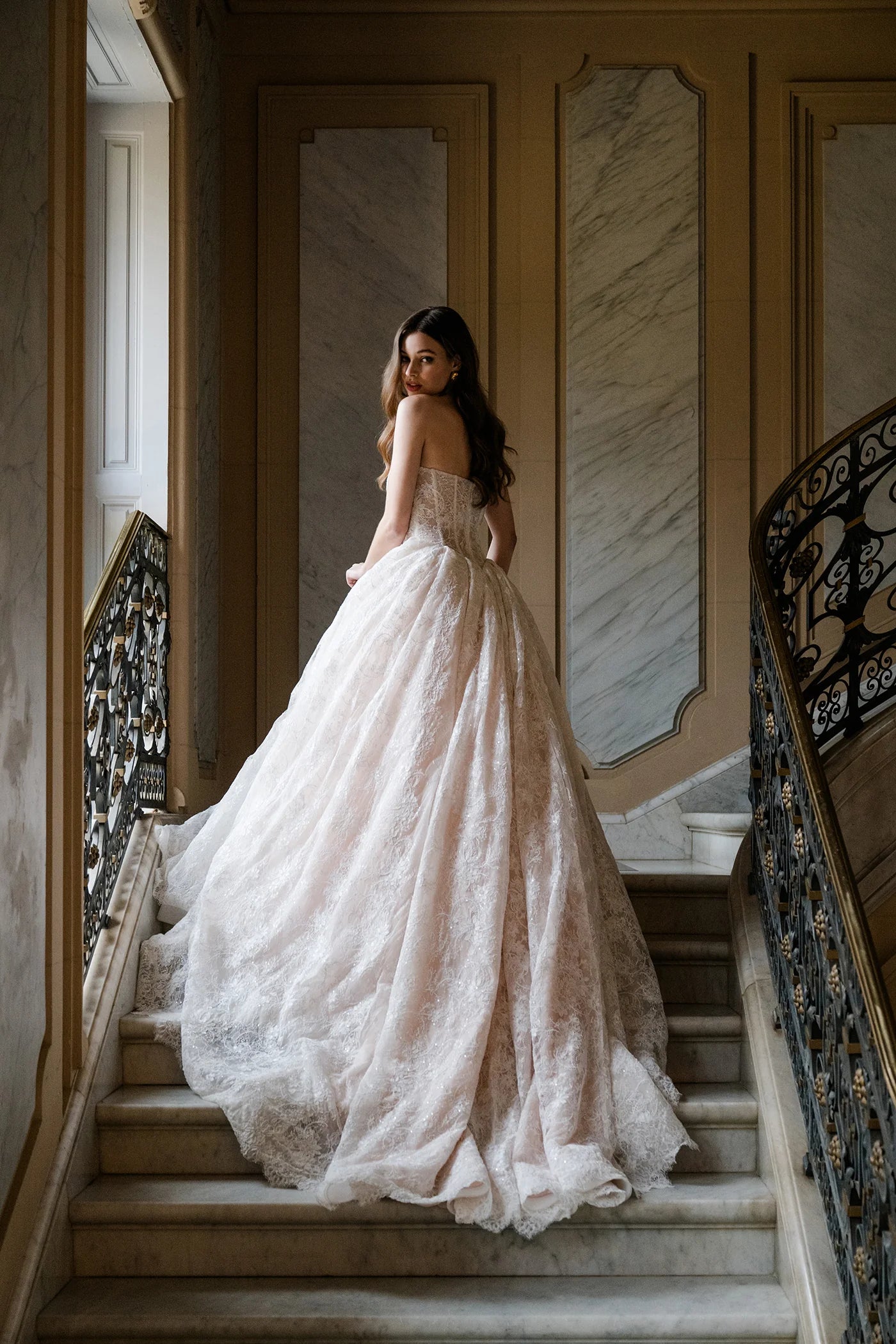 Woman in a white wedding dress standing on a staircase in an elegant interior setting