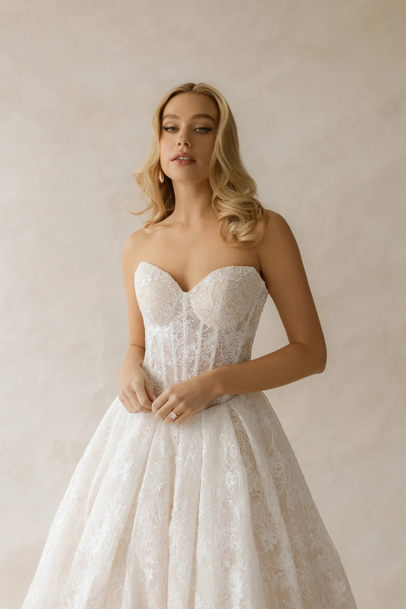 Woman wearing a strapless lace wedding dress against a plain background