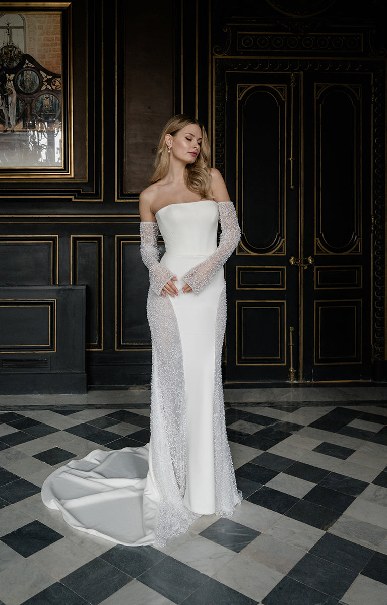 Woman in a white wedding dress standing in an elegant room with dark walls and a checkered floor.