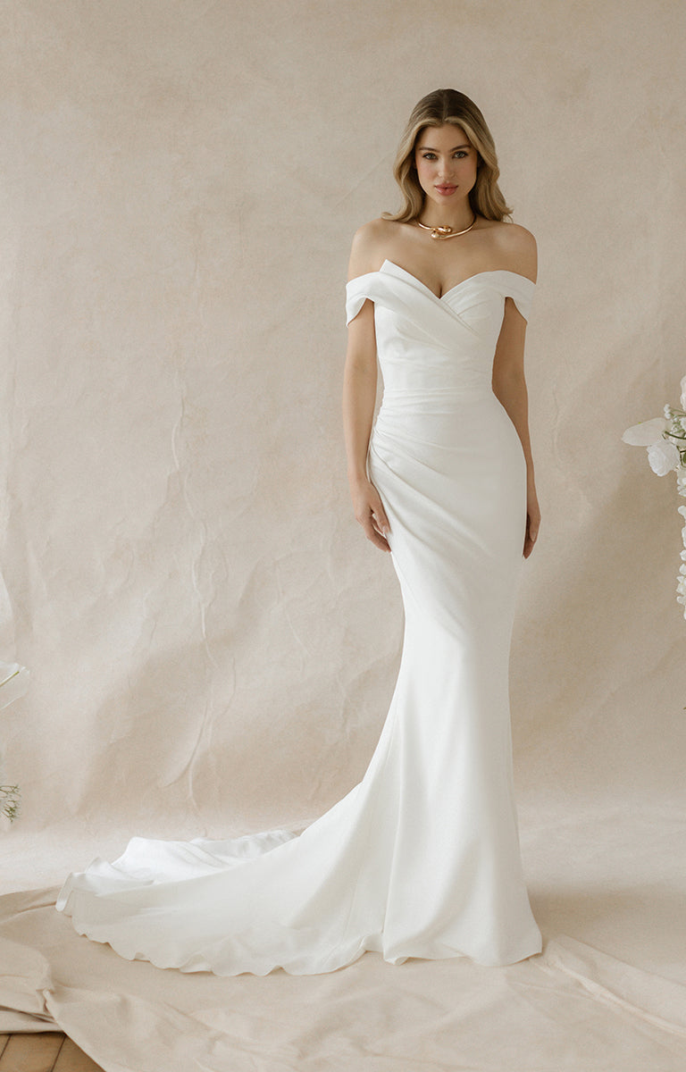 Woman wearing a white off-shoulder wedding dress against a neutral background