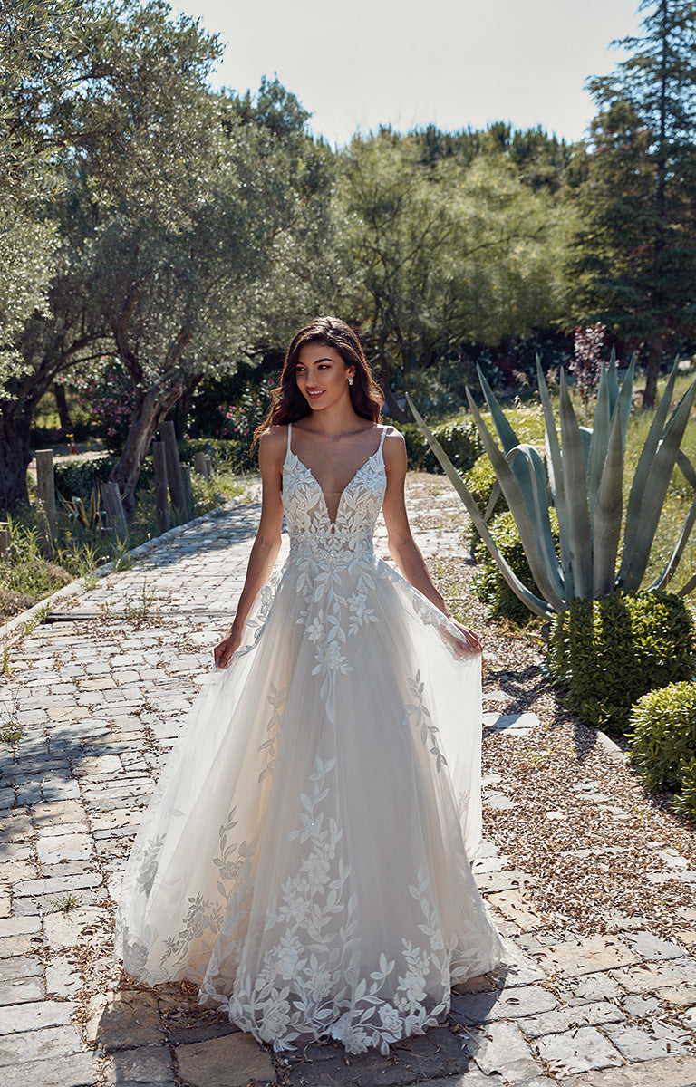 Woman in a white lace wedding dress standing on a stone path with greenery in the background
