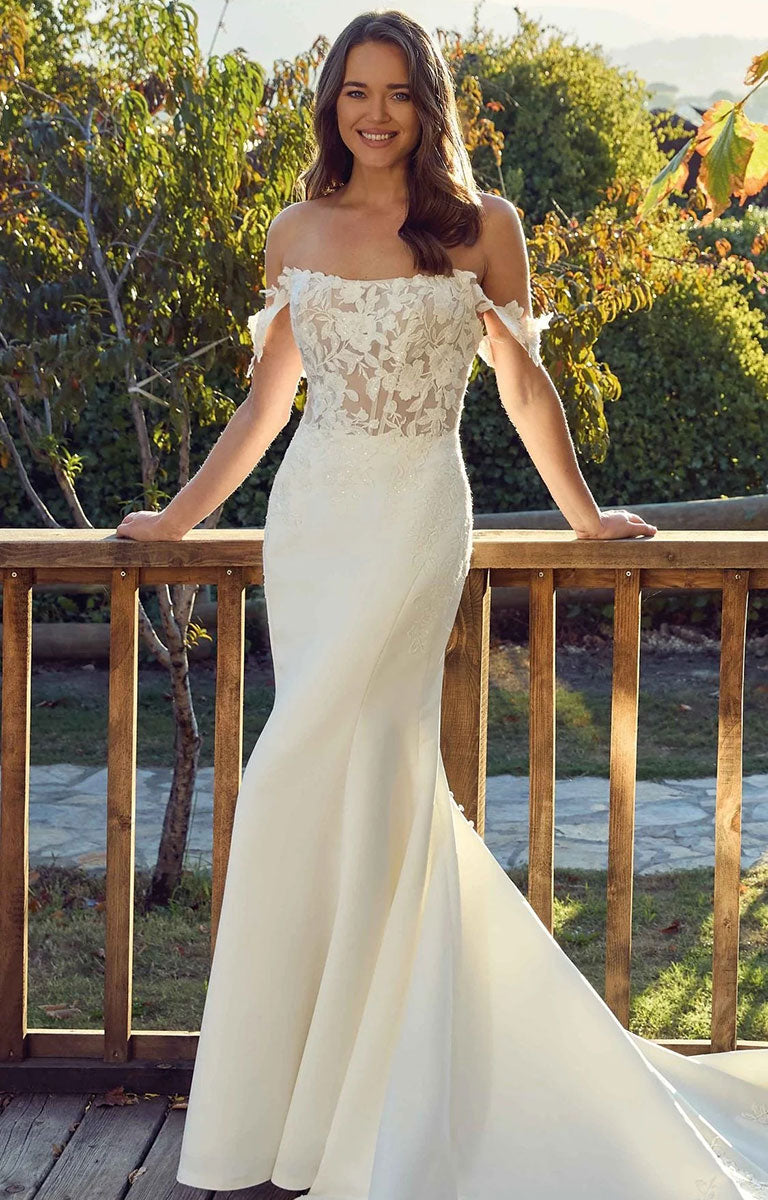 Aspen EK1901 by Eddy K Italia - Satin and Lace Fit-and-Flare Wedding Dress with Cat-Eye Neckline with a lace bodice and satin mermaid skirt, worn by a model standing on a wooden deck with trees in the background.