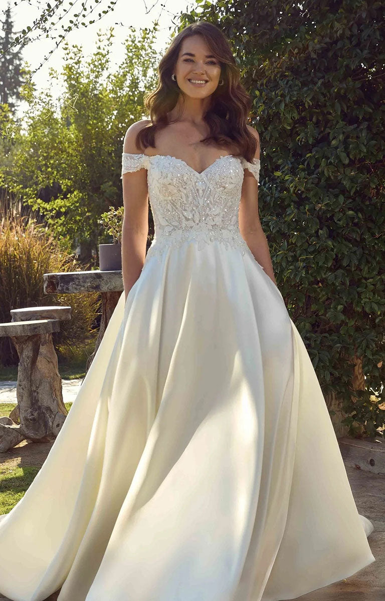 A woman wearing Opalite EK1921 by Eddy K Italia - Mikado Ballgown Wedding Dress with Chantilly Lace with a lace sweetheart bodice and a flowing satin skirt, standing outdoors in a garden setting.