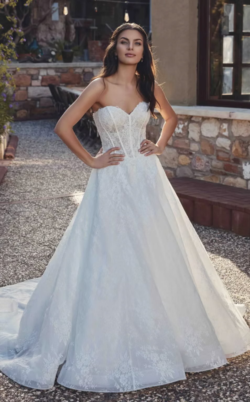 Woman in a white wedding dress standing outdoors with stone walls and plants in the background