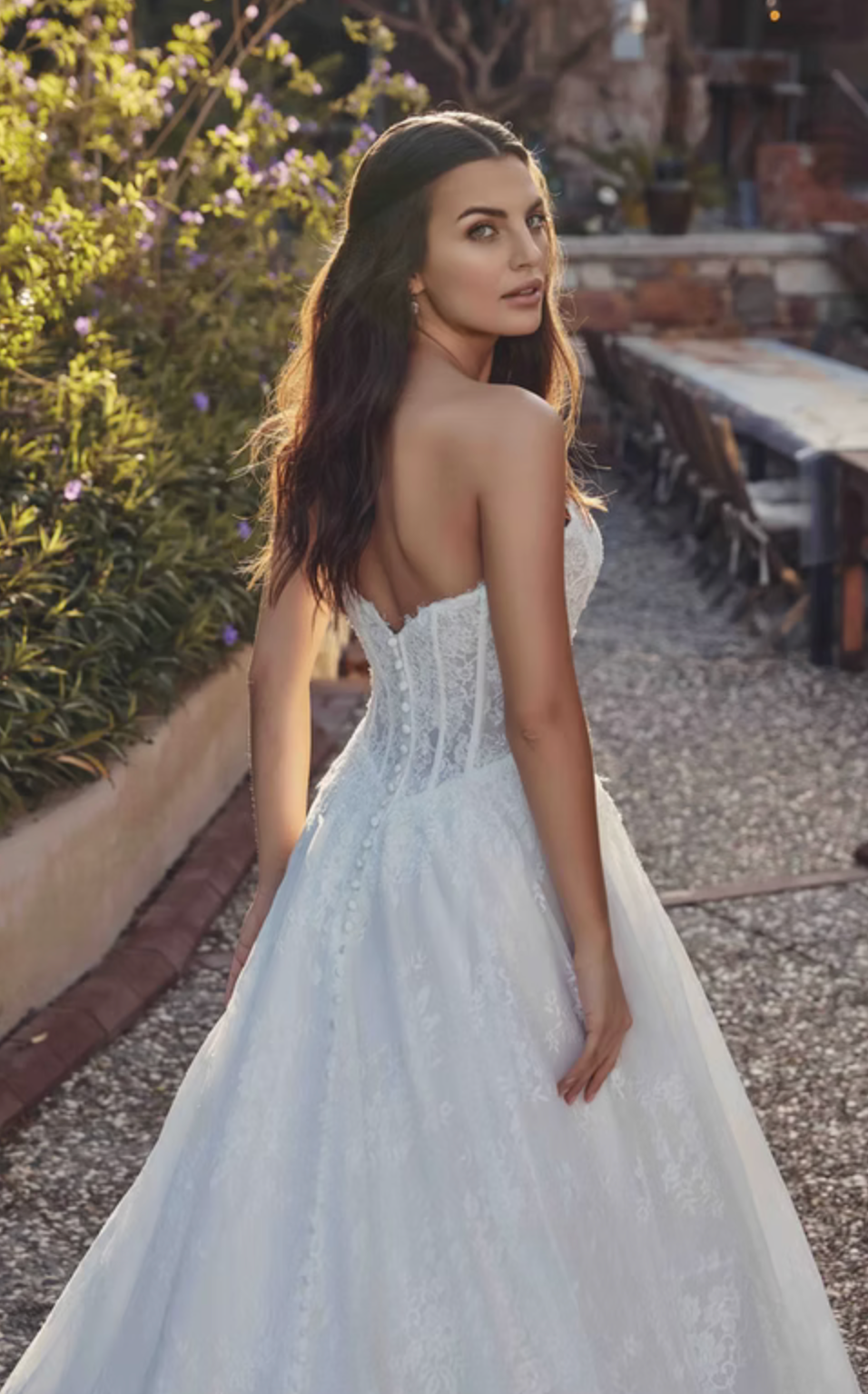 Woman in a white wedding dress standing outdoors with greenery and tables in the background