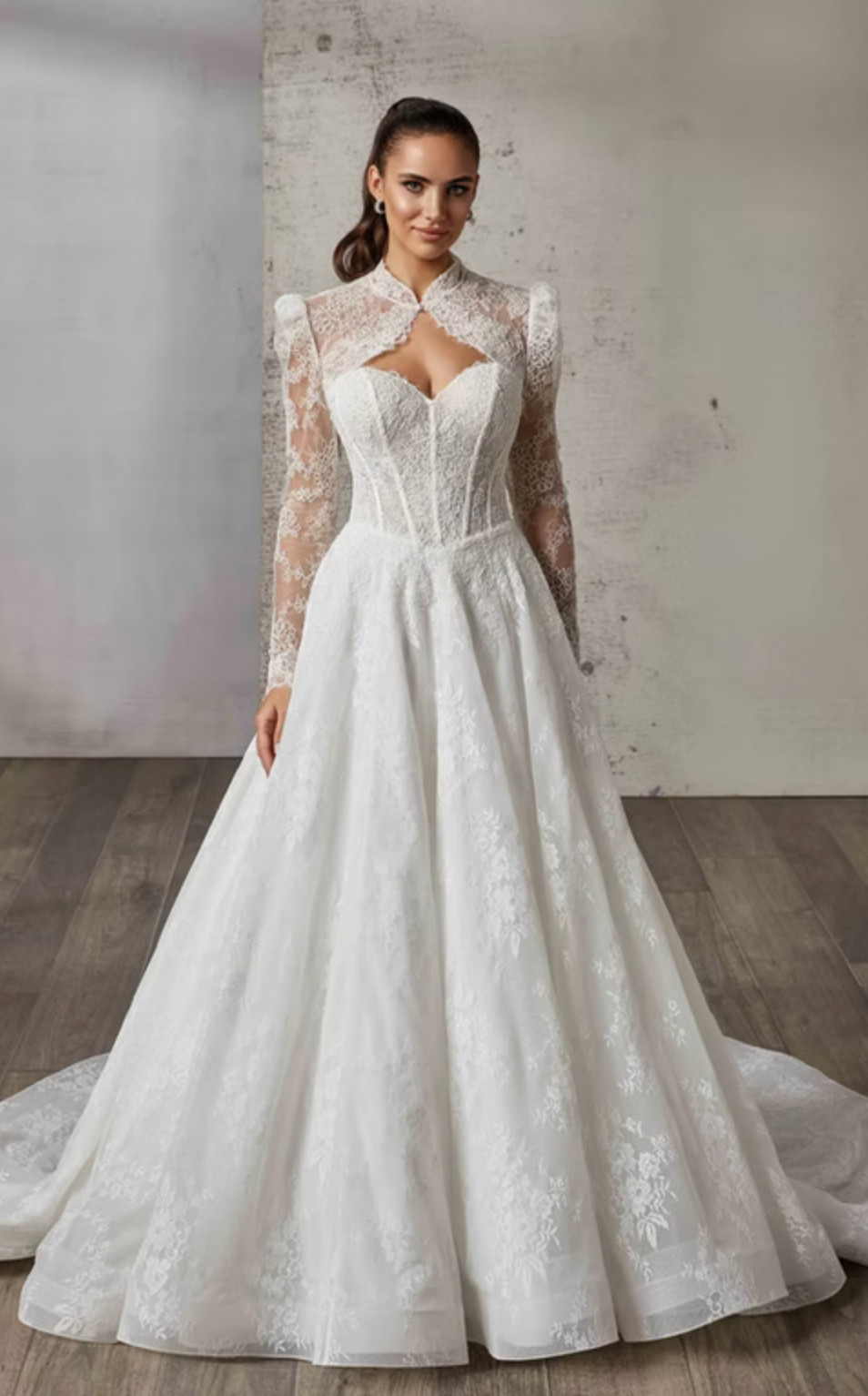 Woman wearing a white lace wedding dress with matching lace jacket in a room with wooden floor and gray walls.