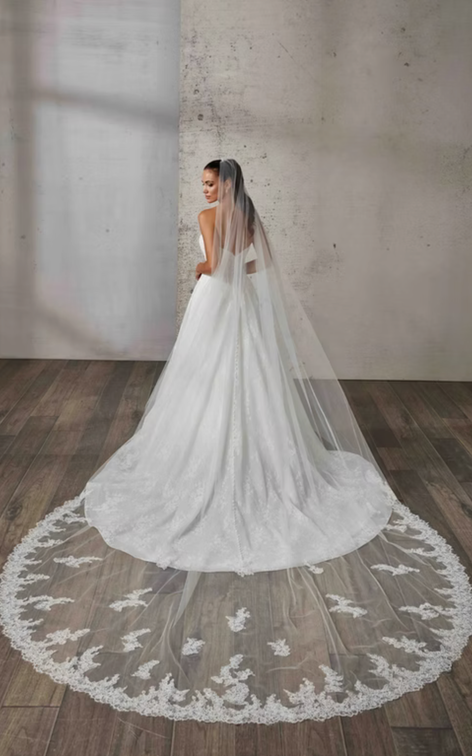 Bride in a white wedding dress with a long veil standing against a textured wall.