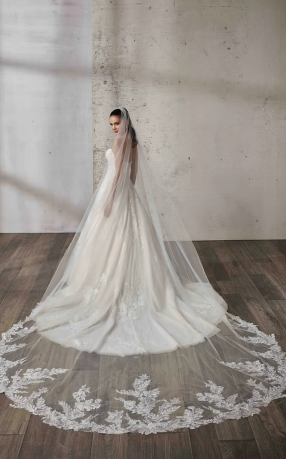 White wedding dress with a long veil on a wooden floor.