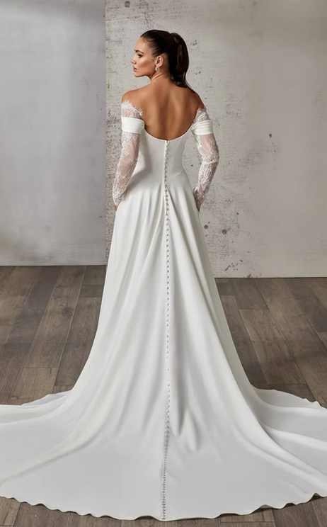 White wedding dress with sheer sleeves and a long train on a wooden floor.