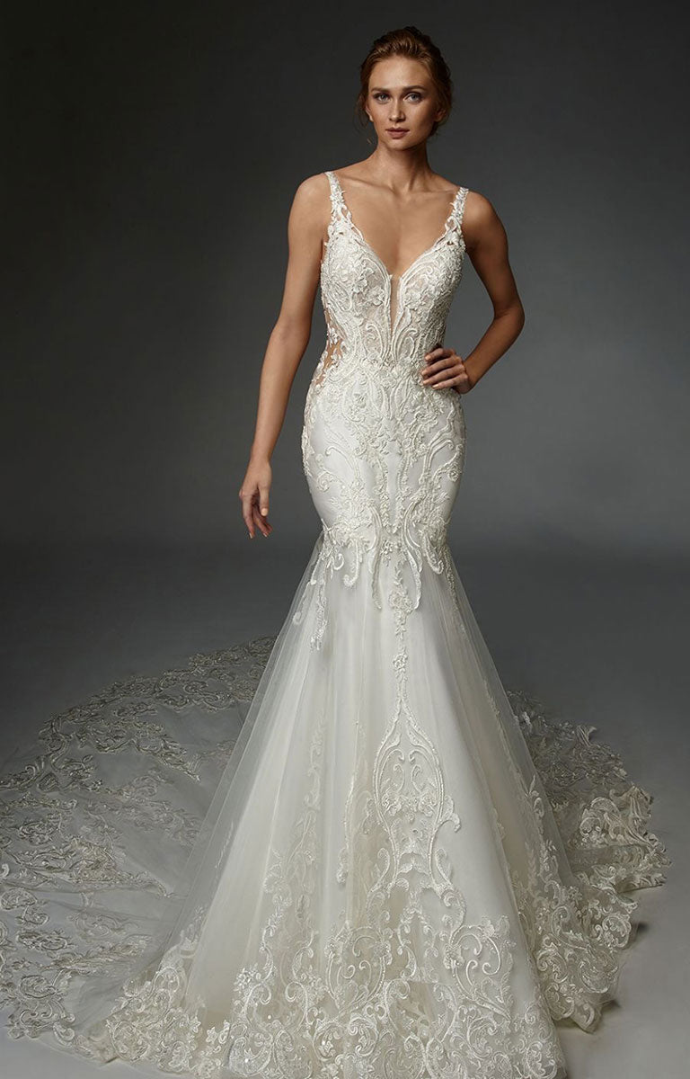 Woman wearing Henriette by ÉLYSÉE - Graphic Lace Wedding Dress with Illusion Bodice and Beaded Detailing against a dark background