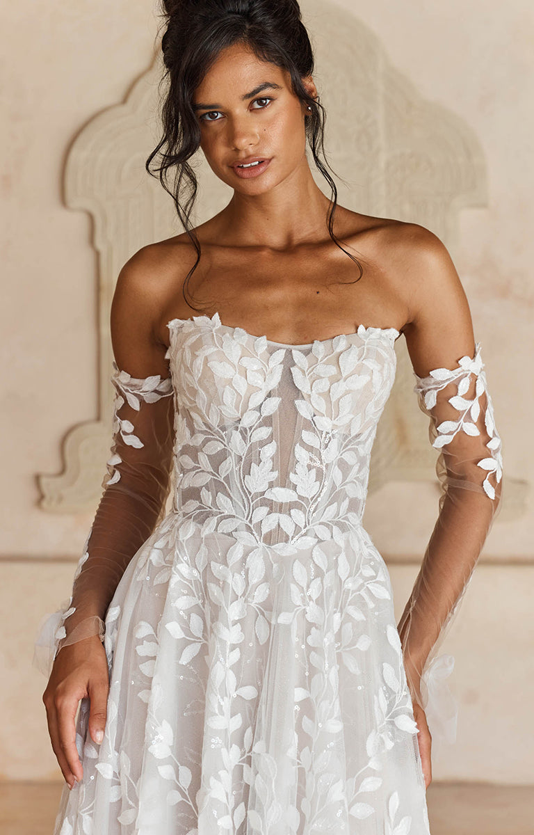 Woman wearing Laiya by Madi Lane, a white floral dress with sheer sleeves in an elegant setting