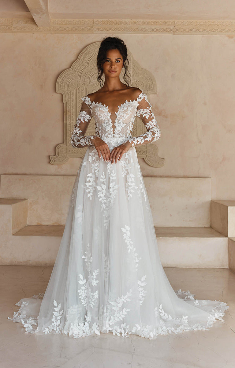 Woman wearing Landon by Madi Lane,  a white wedding dress with floral details in an elegant setting.