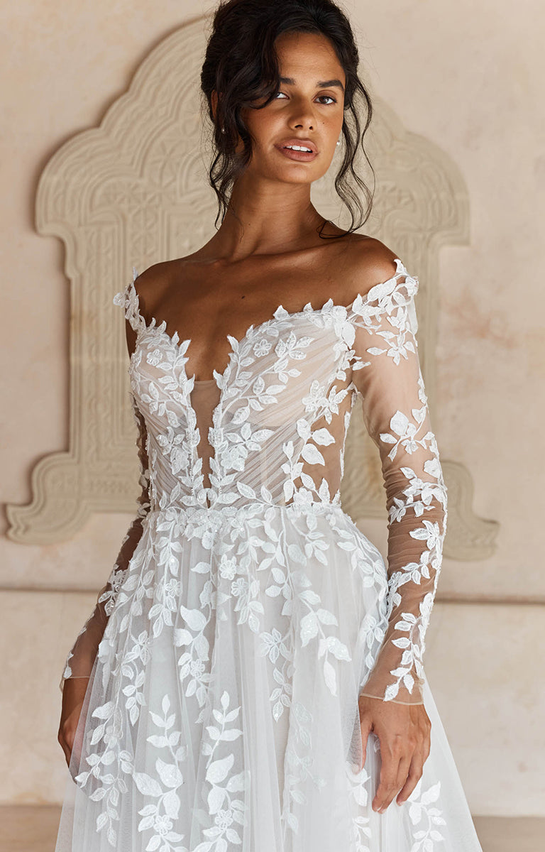 Woman wearing Landon by Madi Lane, a white wedding dress with floral lace details against a neutral background