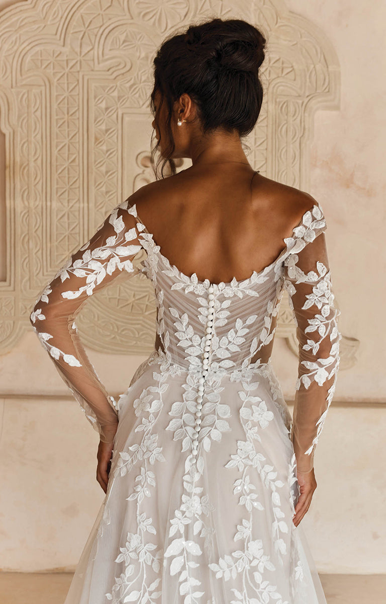 Womans back in Landon by Madi Lane, a white lace wedding dress with long sleeves against an ornate wall.