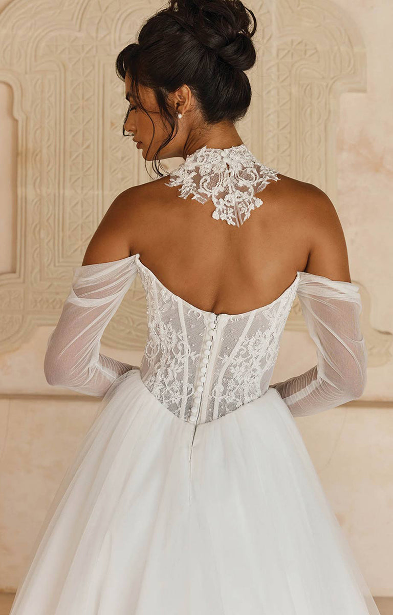 Woman wearing Larkin ML25140 by Madi Lane - Beaded Chantilly Lace Ball Gown with Basque Waist with sheer sleeves in an elegant setting.