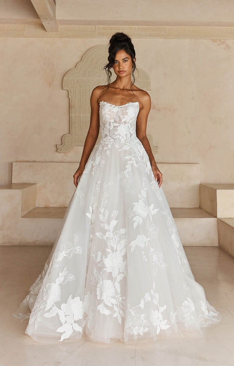 Woman wearing Liana by Madi Lane, a strapless wedding dress with floral details in an elegant setting.