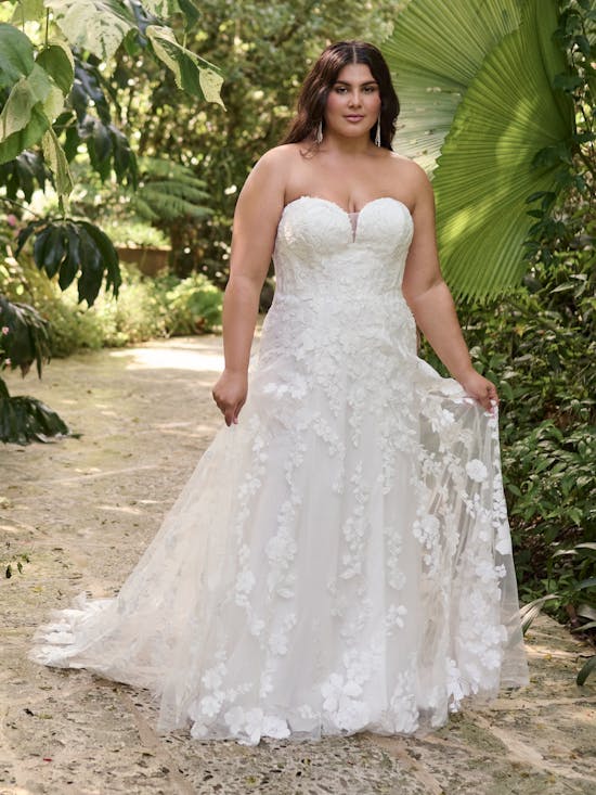Woman wearing Demetria by Maggie Sottero - a strapless wedding gown standing in a natural setting with greenery.