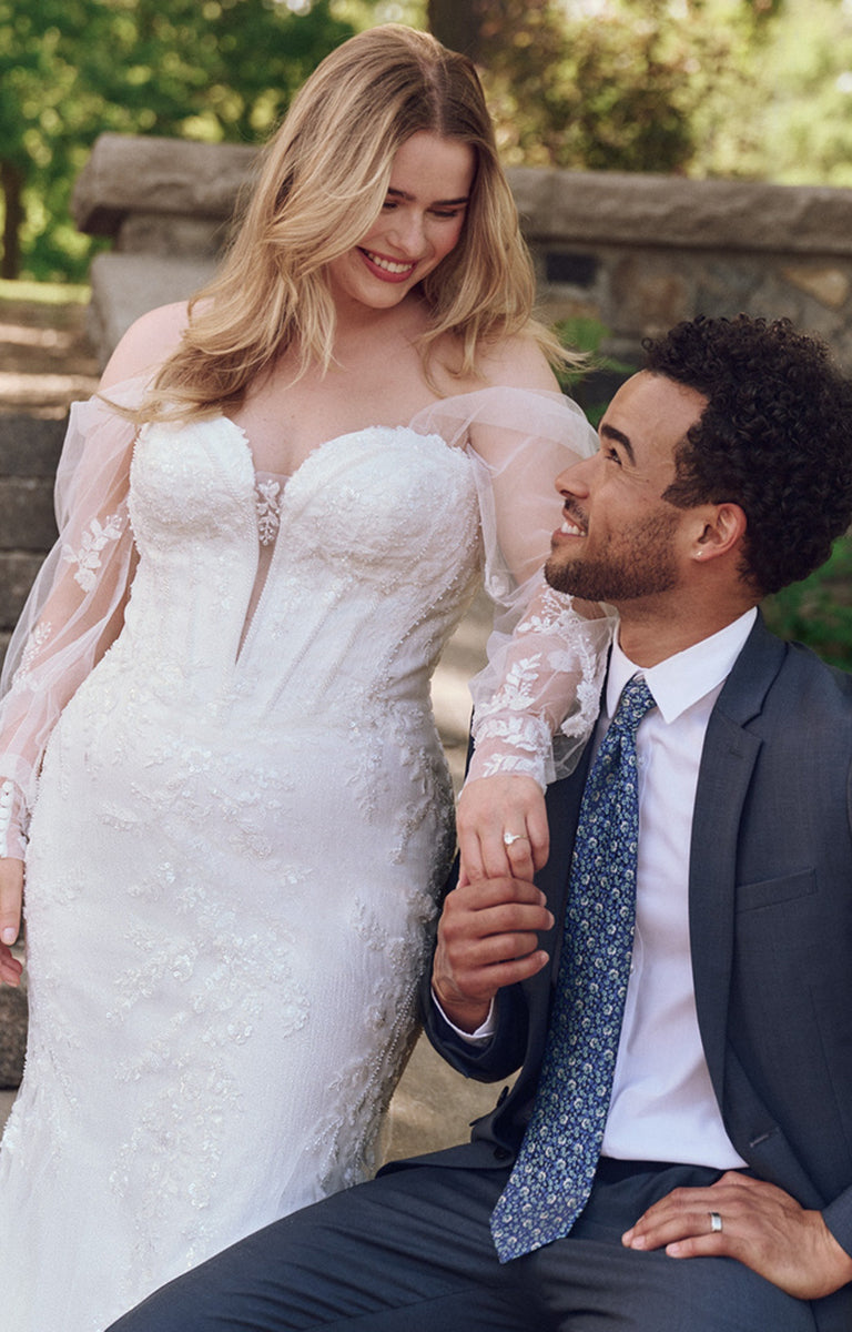 Man and woman in wedding attire sitting together outdoors.