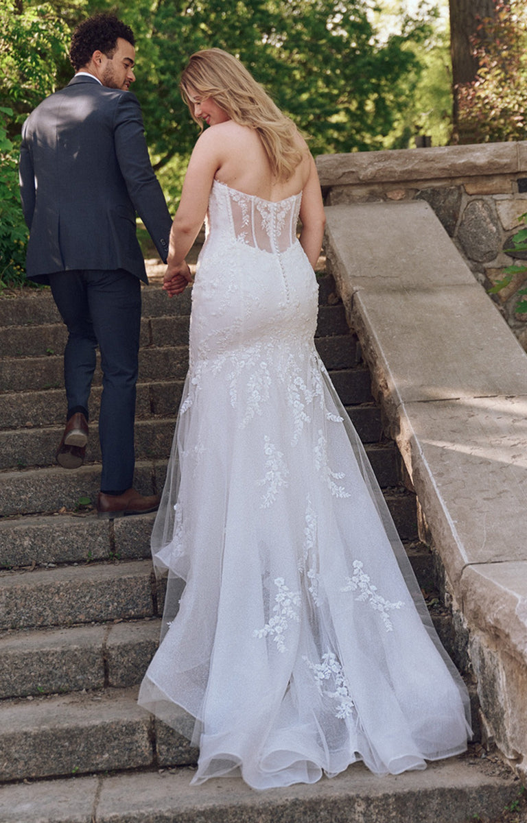 Man and woman holding hands on stone steps, woman in a white wedding dress.