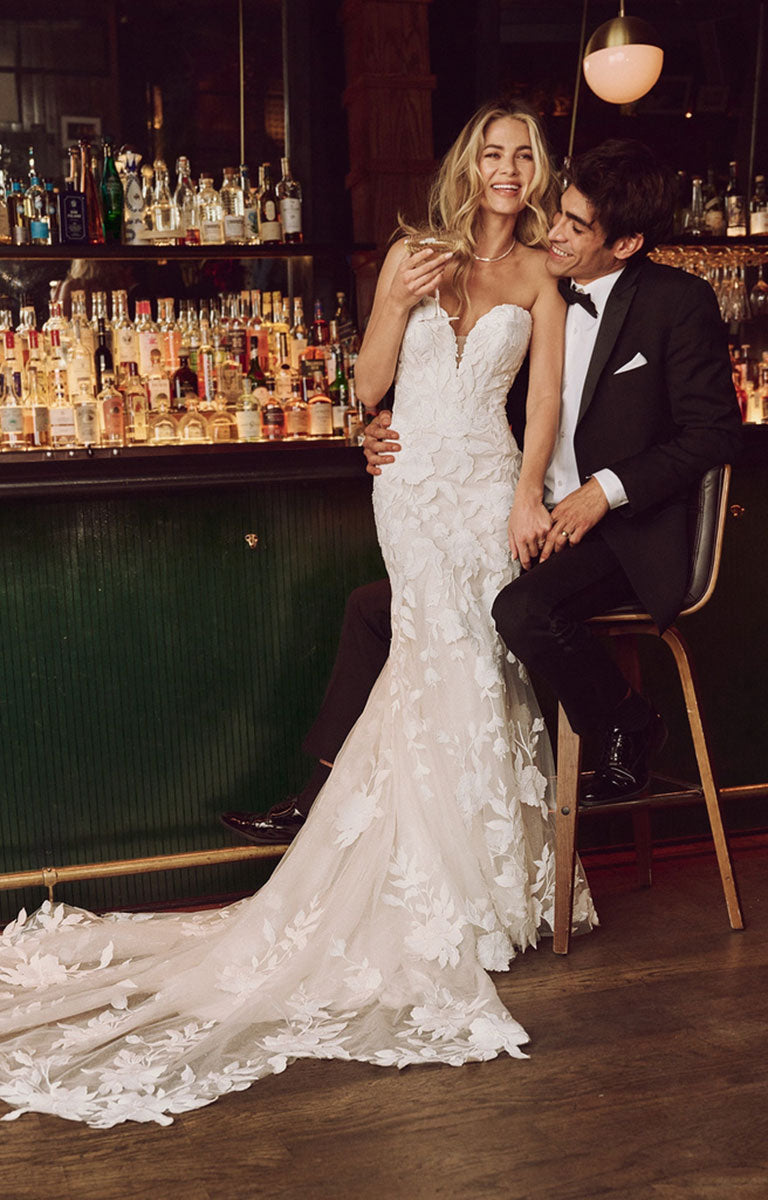 Couple in wedding attire sitting at a bar with bottles in the background