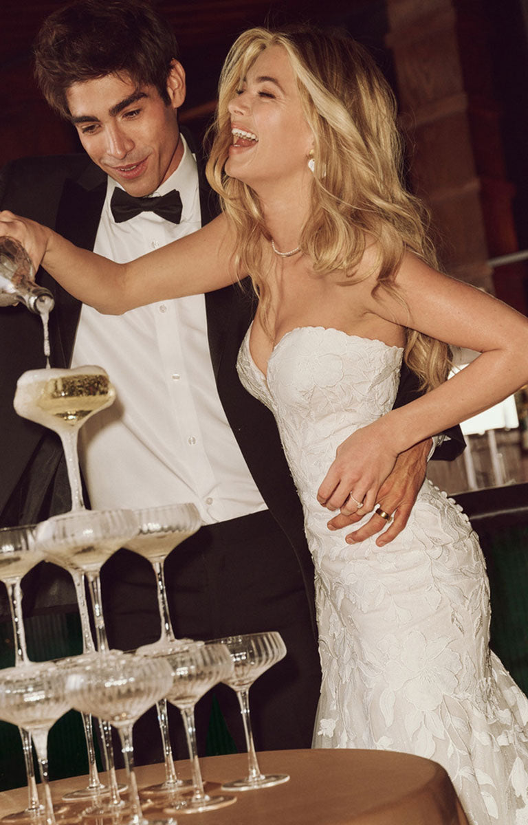 Man in tuxedo pouring a drink for a woman in a white dress at a formal event.