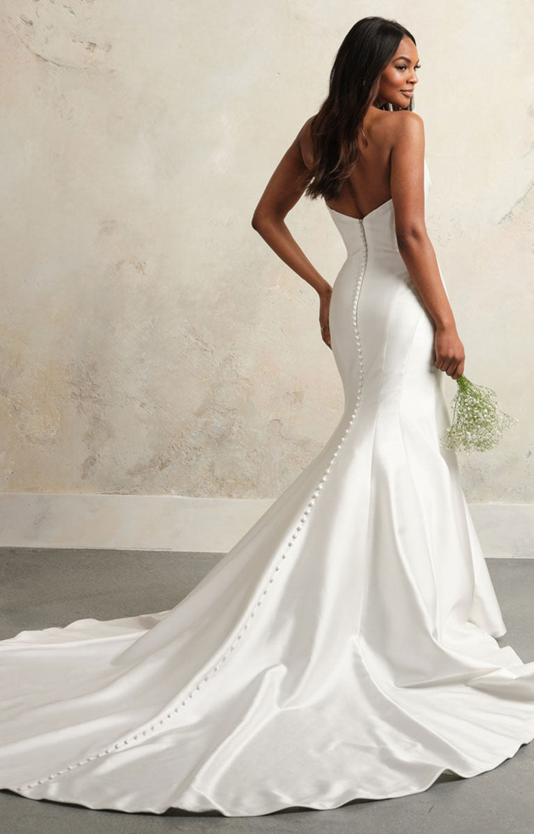Woman in a white wedding dress holding a bouquet against a neutral background