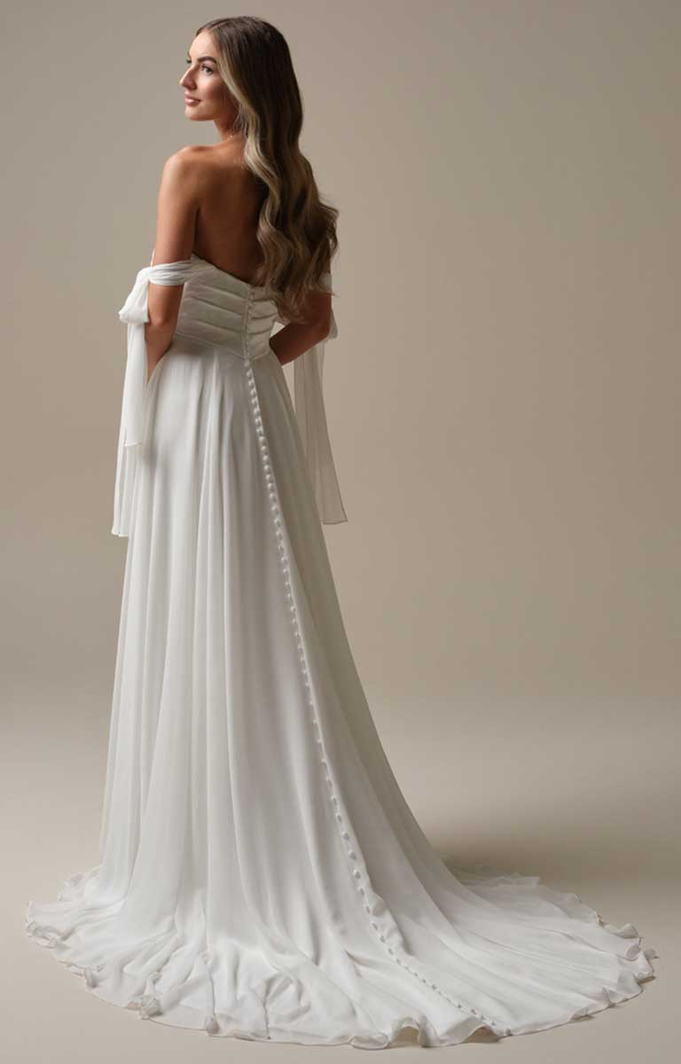 Woman wearing a white off-shoulder dress with long sleeves against a beige background