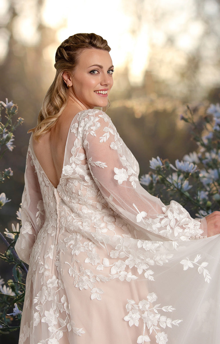 Woman in a floral dress standing among flowers with a blurred natural background
