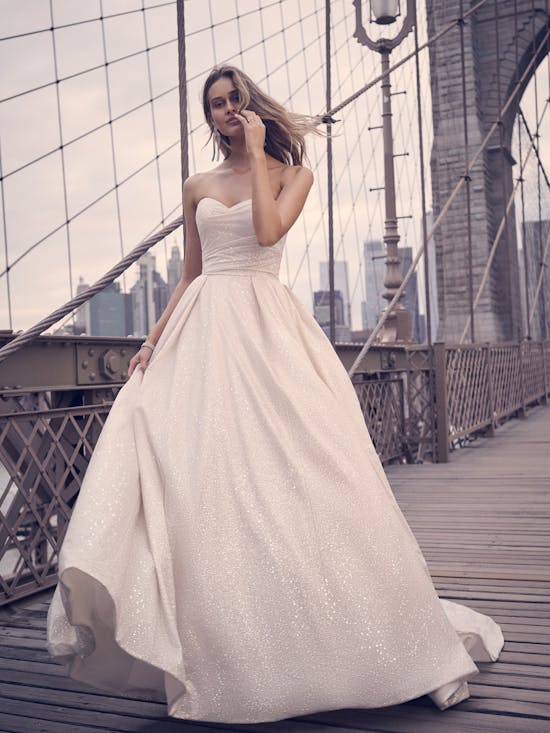 Woman in a white wedding dress standing on a bridge with a city skyline in the background