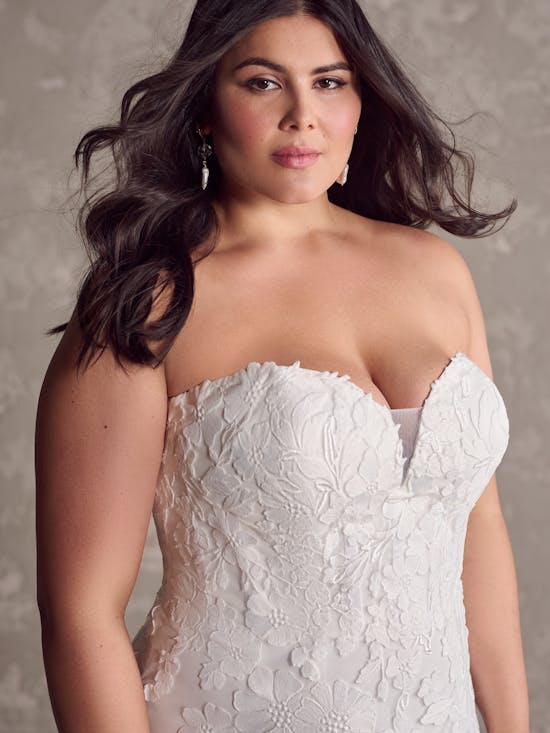Woman wearing Demetria by Maggie Sottero - a white lace wedding dress against a neutral background