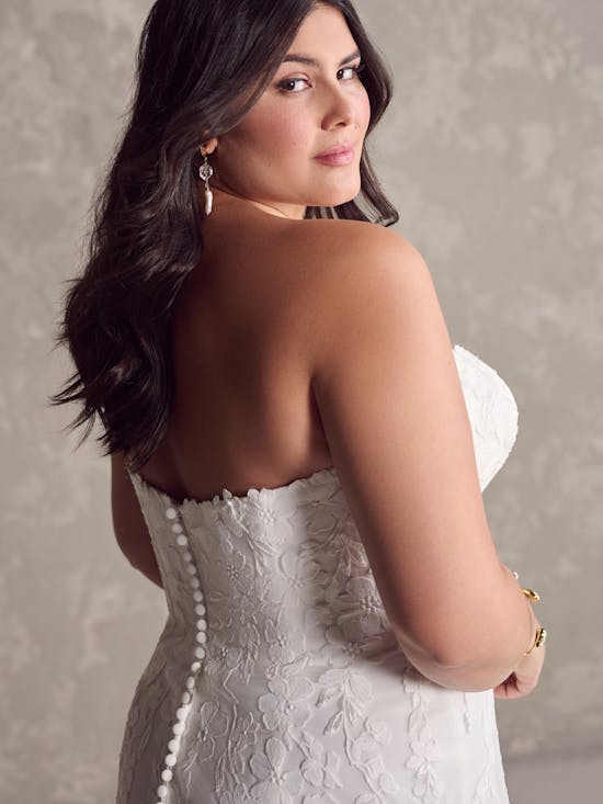 Woman wearing Demetria by Maggie Sottero - a white lace dress with a neutral background