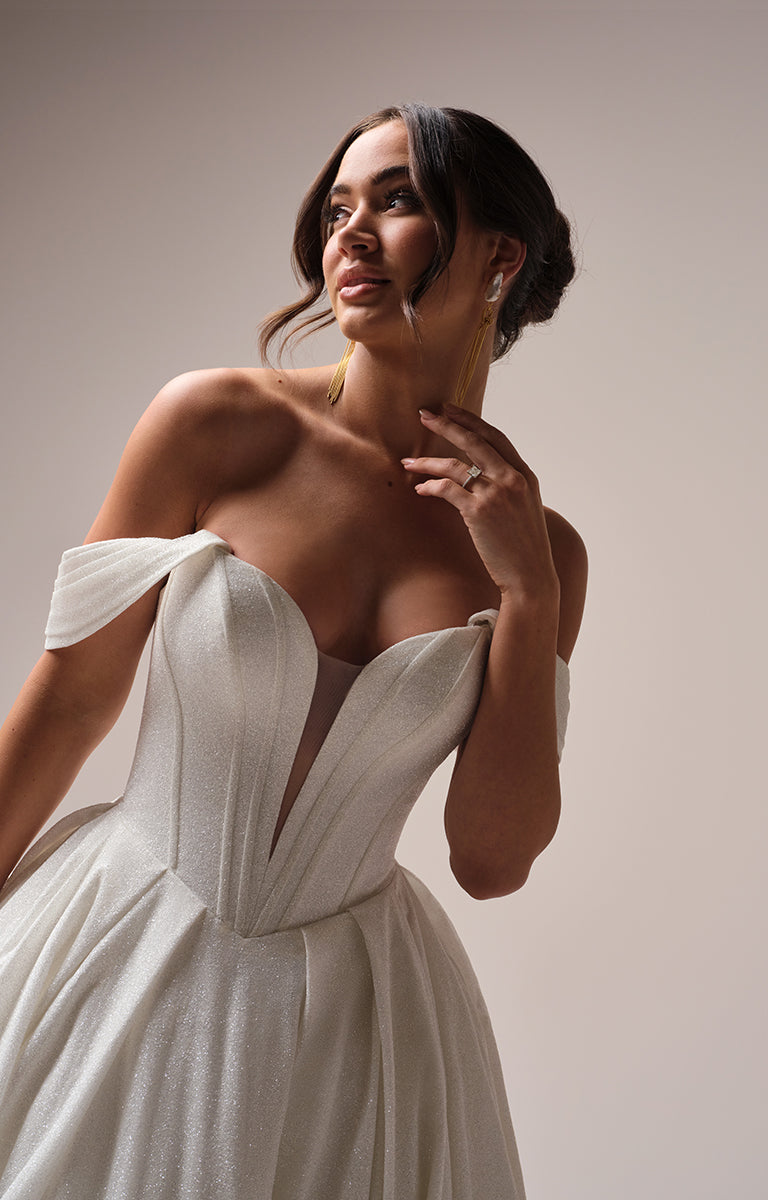 Woman wearing Derrick Royale by Maggie Sottero - an ivory off-shoulder dress against a neutral background