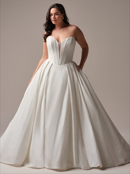 Woman wearing a Derrick Royale by Maggie Sottero - white strapless gown against a plain background