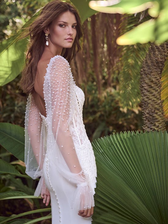Woman in a white dress with sheer sleeves standing among tropical plants