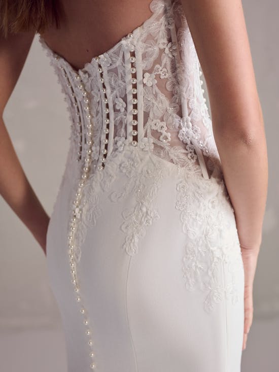 Close-up of a white lace wedding dress with gold accents on a neutral background