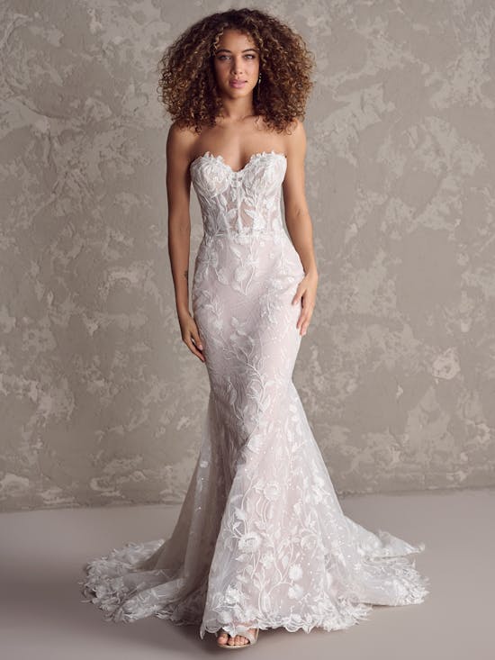 Woman wearing Fairchild by Maggie Sottero - a strapless lace wedding dress against a textured gray background