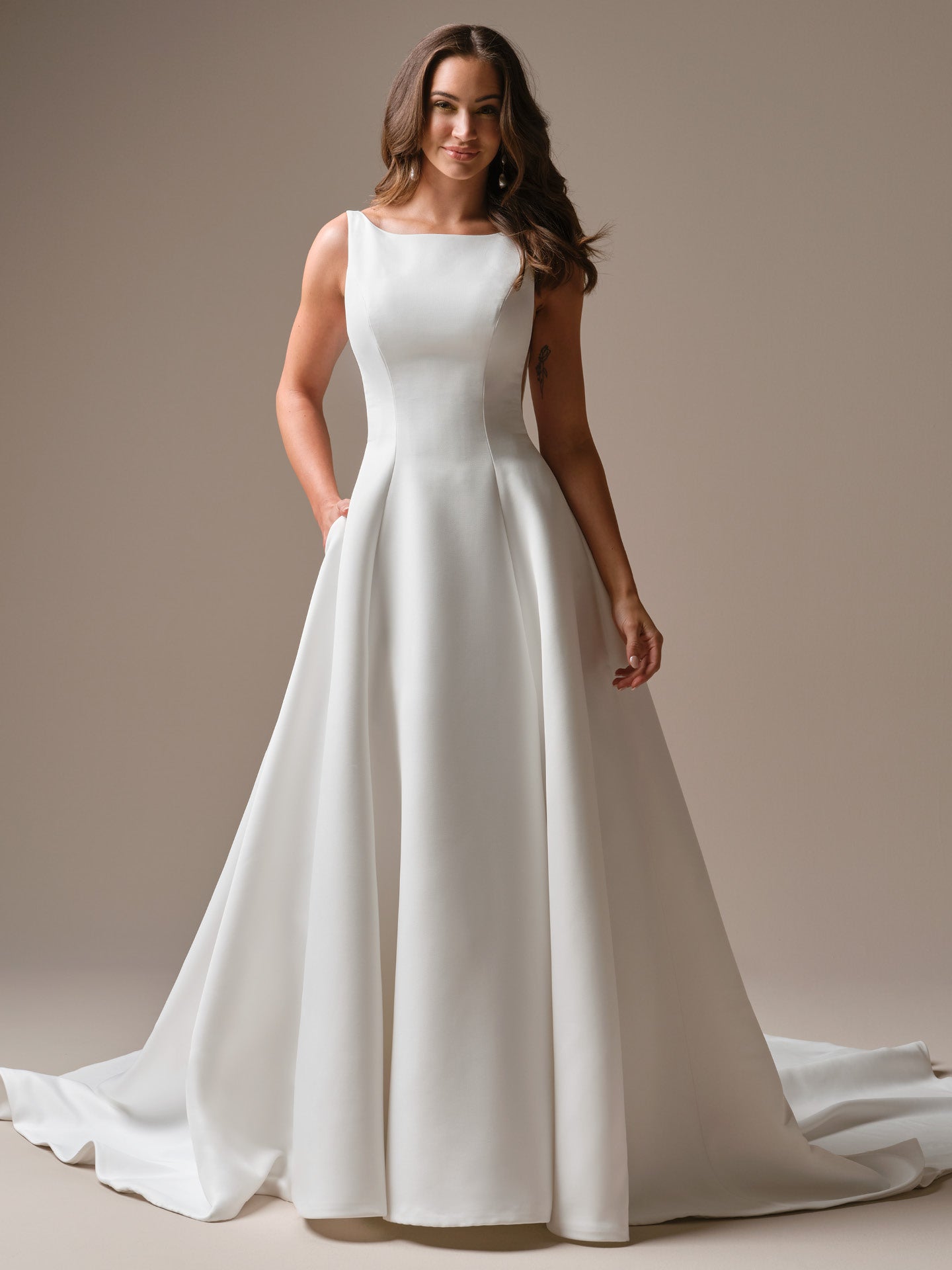 Woman wearing Lawrence by Maggie Sottero - Satin A-Line Wedding Dress with Bateau Neck and Deep V-Back against a neutral background 