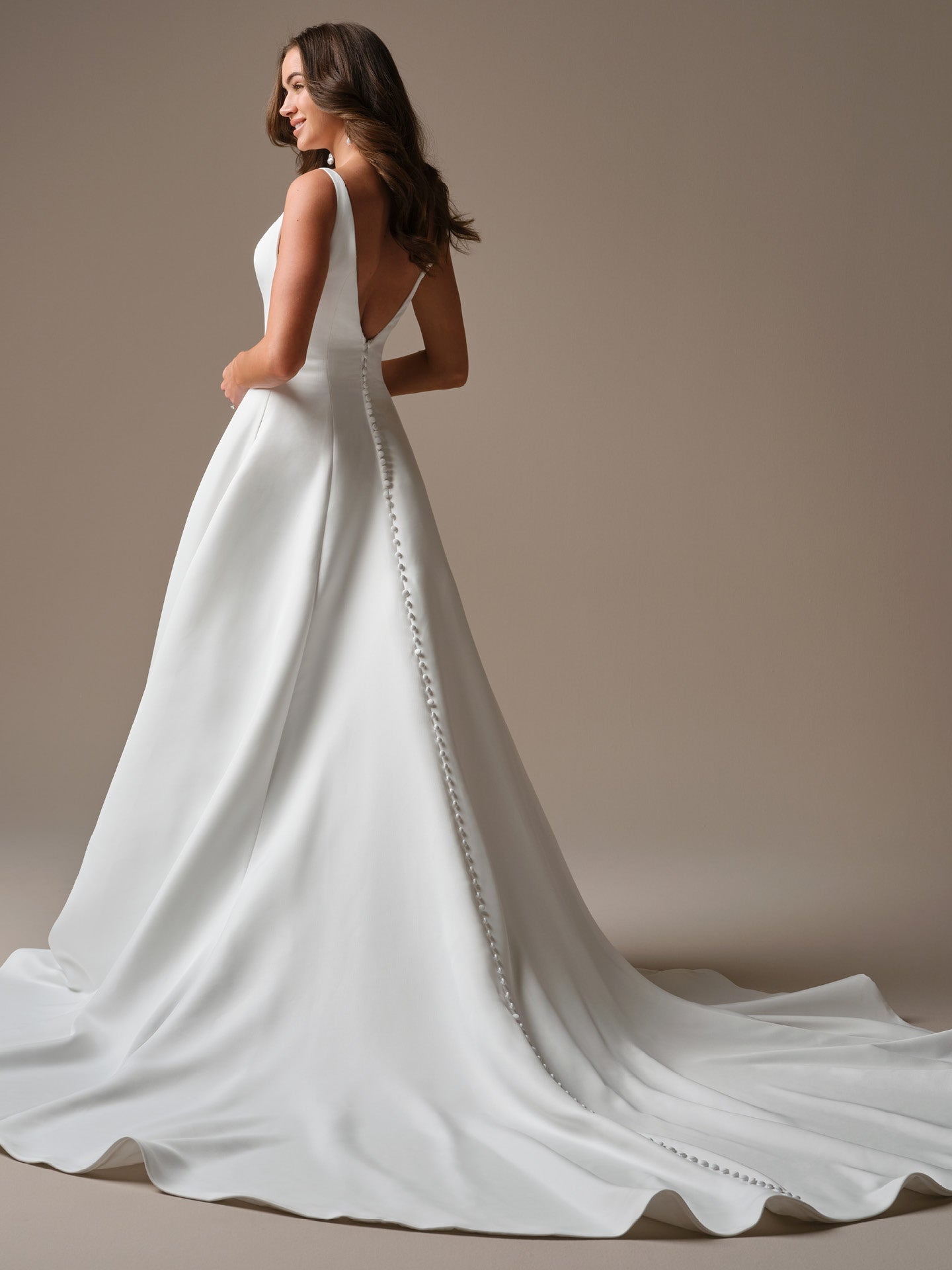 Woman wearing Lawrence by Maggie Sottero - Satin A-Line Wedding Dress with Bateau Neck and Deep V-Back against a neutral background with a long train on a plain background