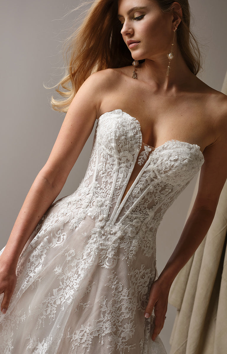 Woman wearing Lucca by Maggie Sottero - Beaded Lace Illusion Bodice A-Line Wedding Dress against a neutral background