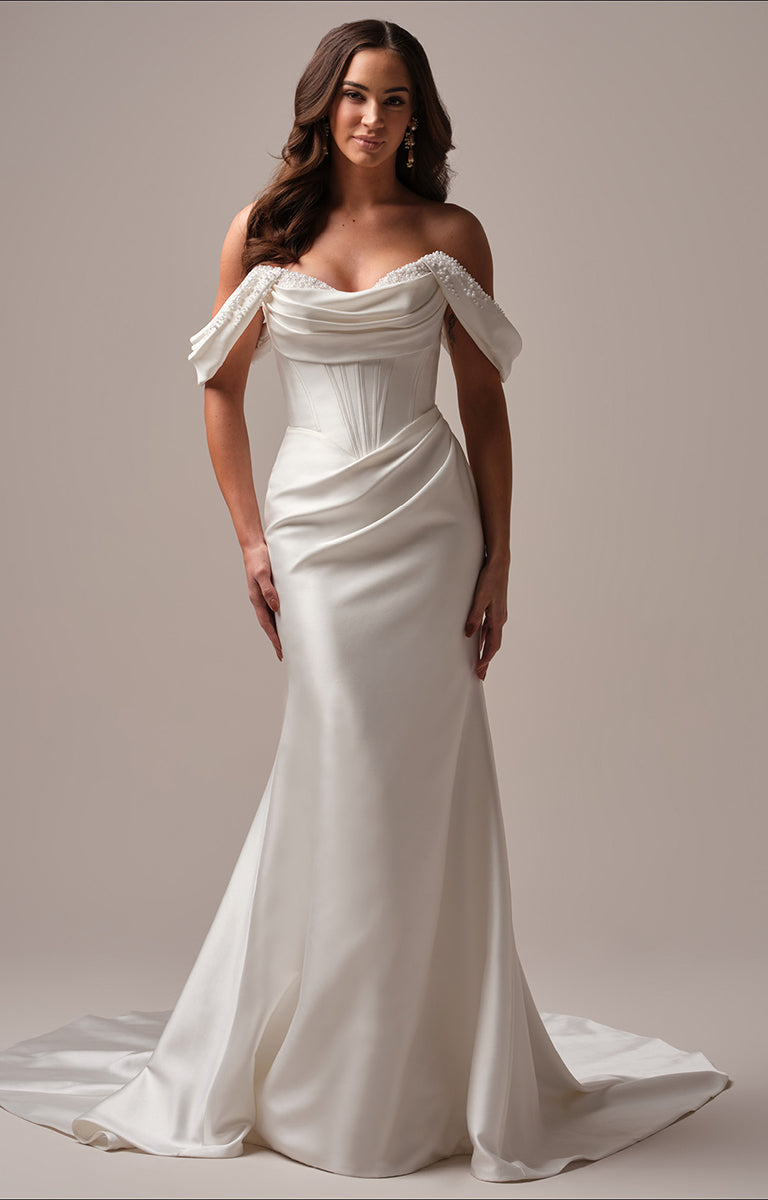 Woman wearing Melissa fit and flare wedding dress by Maggie Sottero - a white off-shoulder gown against a plain background