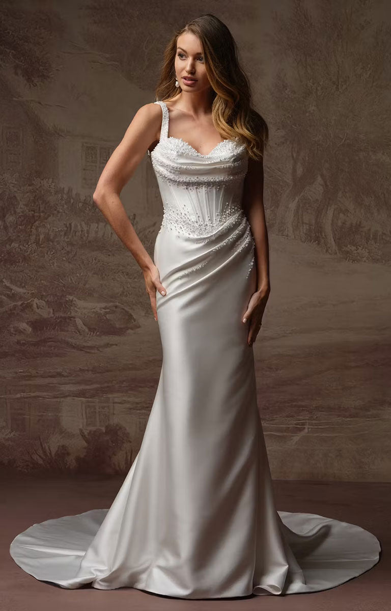 A woman modeling Melissa Marie Royale by Maggie Sottero - Pearl-Embellished Draped Satin Wedding Dress with a fitted bodice, beaded waist, draped skirt, and train, posed against a warm brown scenic backdrop.