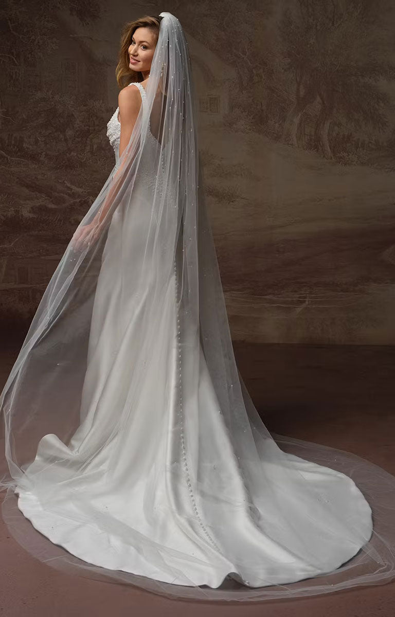 A woman wearing Melissa Marie Royale by Maggie Sottero - Pearl-Embellished Draped Satin Wedding Dress with a long sheer veil, posed against a textured brown studio backdrop.