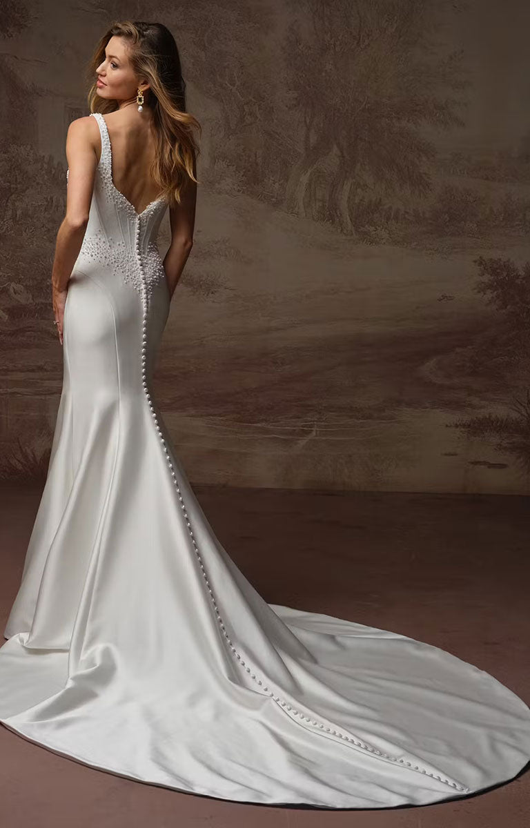 A woman modeling Melissa Marie Royale by Maggie Sottero - Pearl-Embellished Draped Satin Wedding Dress from the back, showing a satin mermaid-style dress with a deep V back, beaded embellishment down the spine, and a long train against a warm brown studio backdrop.