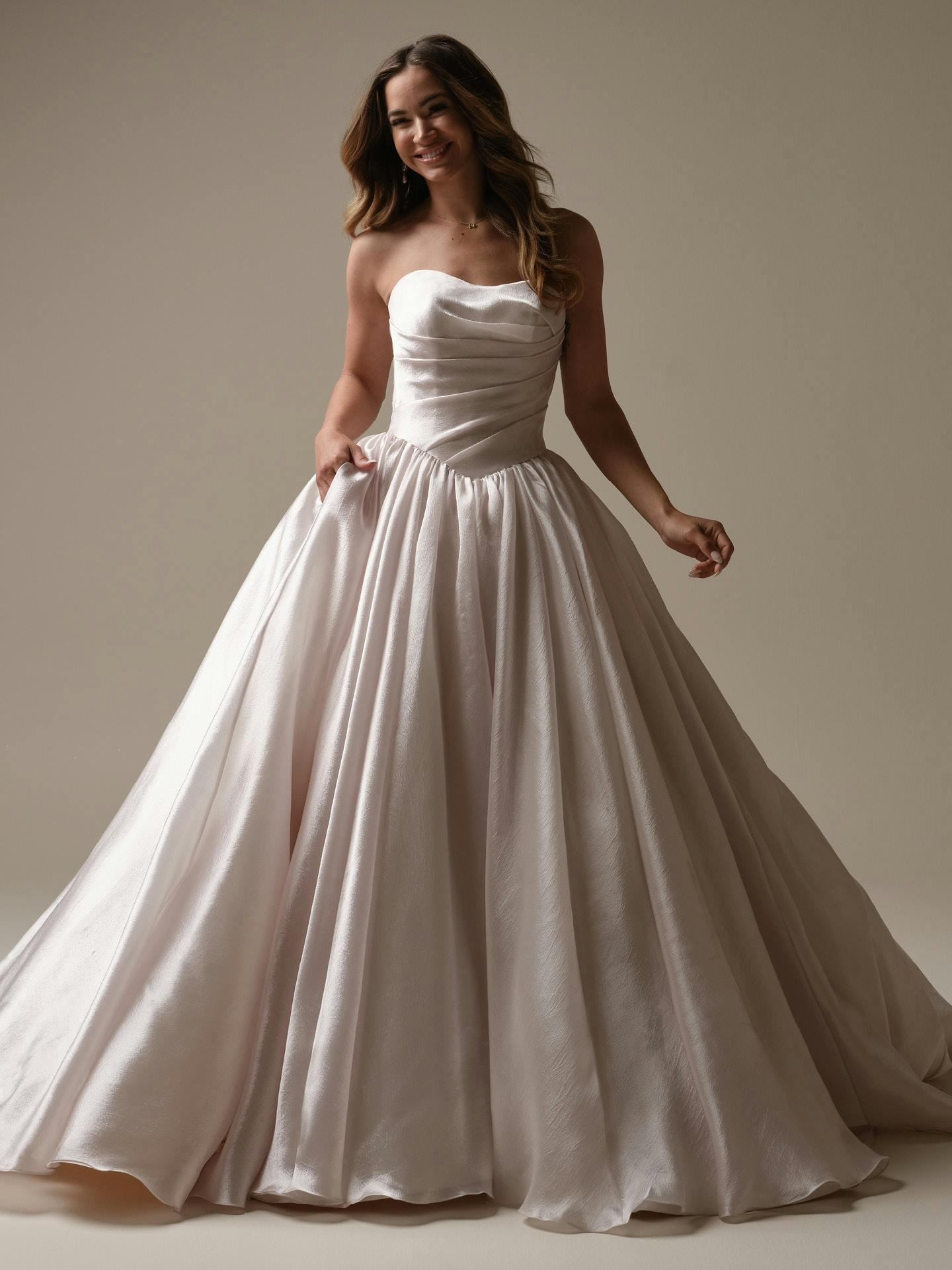 Woman wearing Paris by Maggie Sottero - a strapless white wedding dress against a plain background