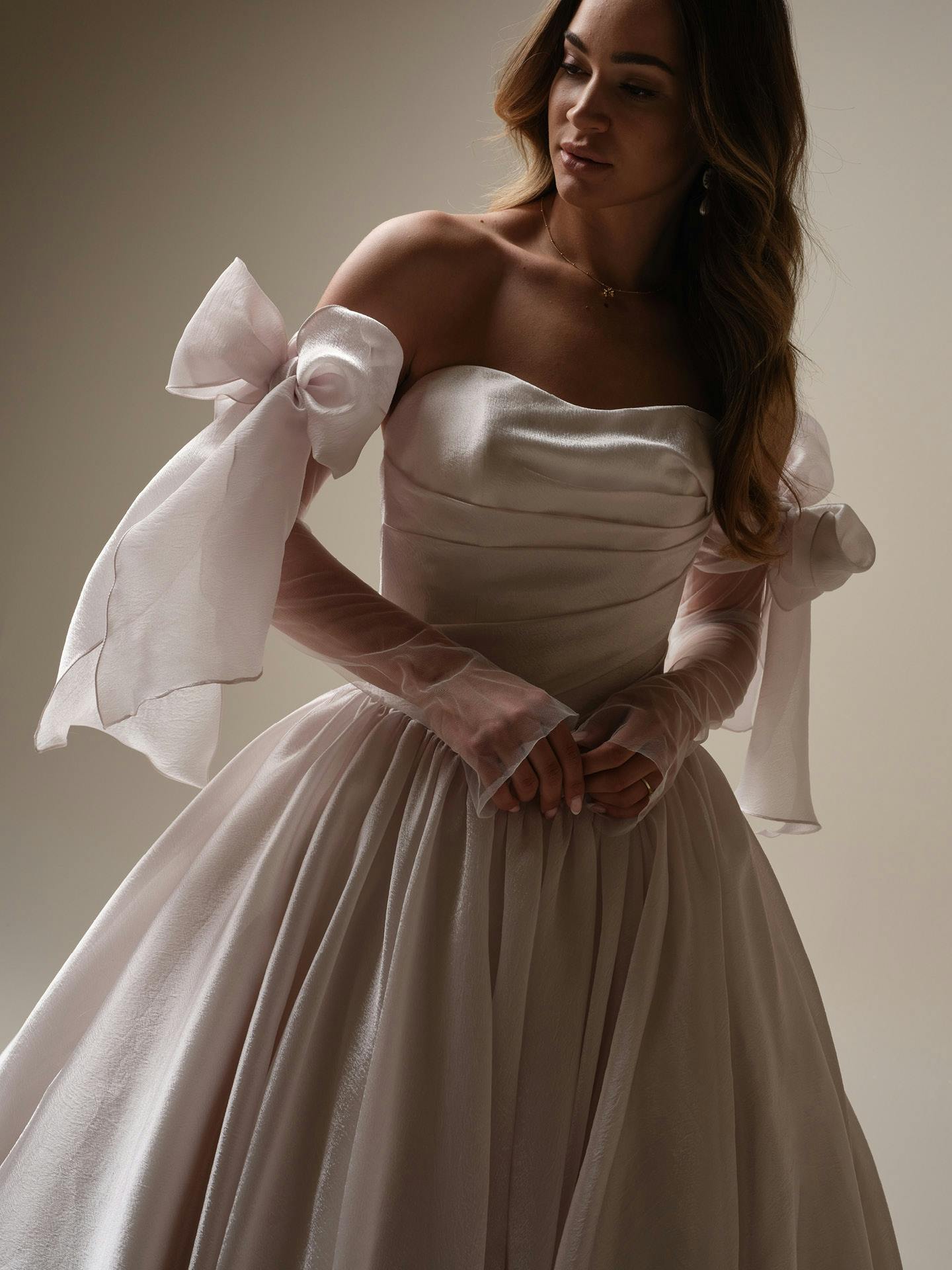 Woman wearing Paris by Maggie Sottero - a white wedding dress with large bows and sheer sleeves.