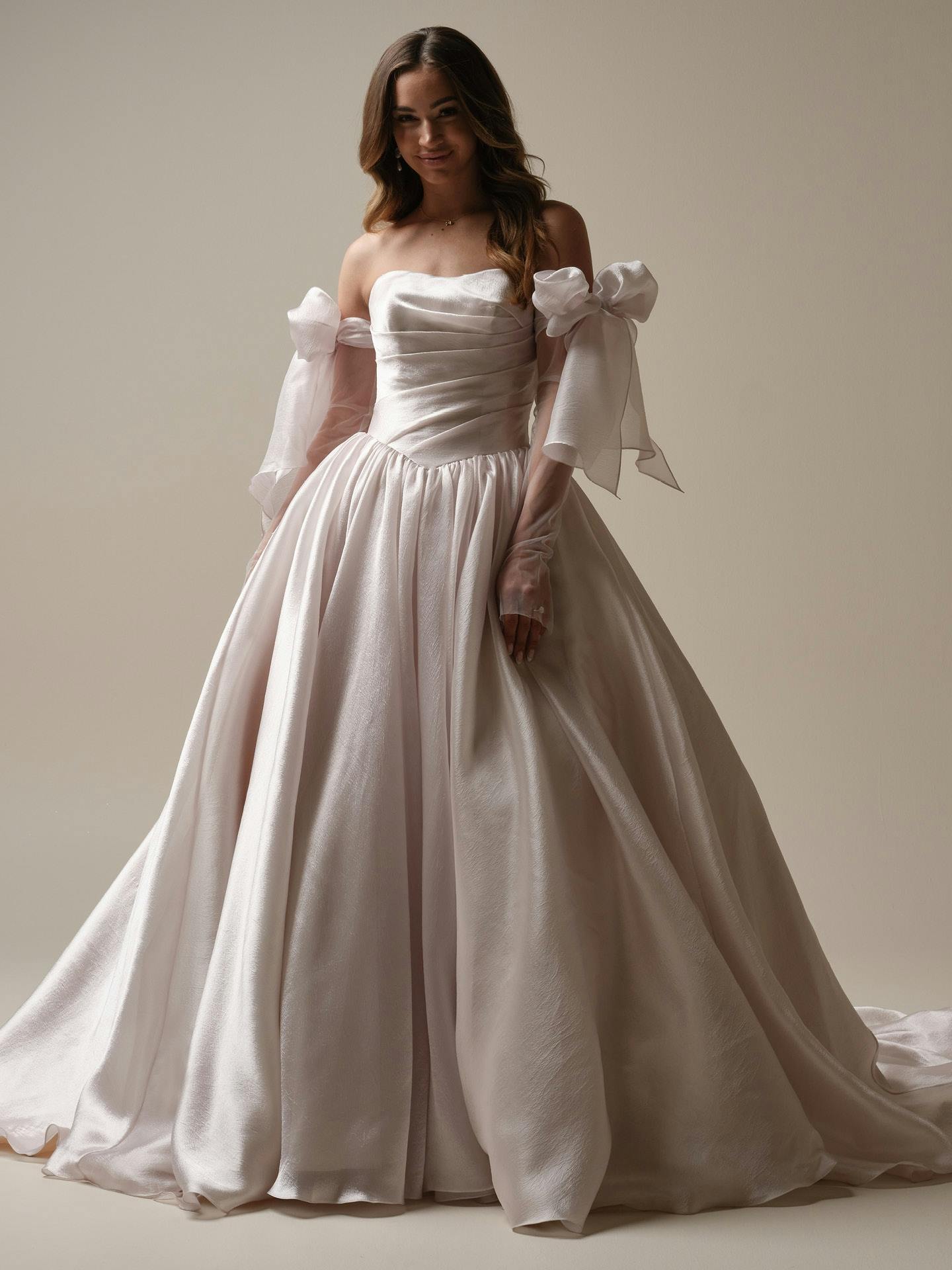 Woman wearing Paris by Maggie Sottero - a white wedding dress with a large bow on a plain background